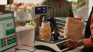 Merchant using scale at cash register checkout in organic shop, weighting freshly harvested fruits and veggies from local farm. African american seller preparing homegrown produce, eco friendly. photo