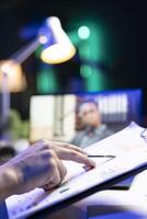 Closeup of person reviewing information on the clipboard while being part of virtual meeting on laptop. Selective focus of an individual checking charts and graphs while on call. photo