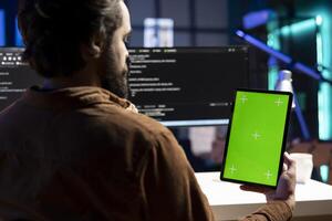Programmer designing and developing software applications using green screen tablet. IT administrator implementing and maintaining company systems using chroma key device photo