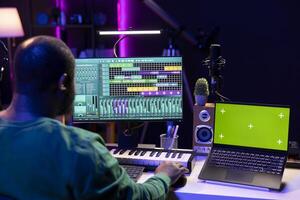 Music producer mixing and mastering songs on digital post production pc interface, greenscreen display. Artist adding sound effects and adjusting volume levels to produce new music. photo