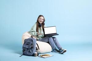 Smiling woman presenting laptop with isolated screen display, doing advertisement, blue studio background. Cheerful person creating ad promotion with mockup notebook device photo