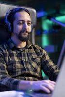 Male individual wearing wireless headphones while browsing the internet on his digital laptop. Closeup of man using portable computer and listening to podcasts on audio headset. photo