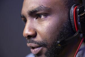 Close up of focused man playing videogame on powerful computer during online gaming championship, talking into headset. African american gamer taking part in Esports team, competing in game photo