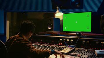 Audio technician works on music post production with greenscreen in control room, pushing sliders and faders to adjust volume level. Producer mixing and mastering tracks with console in studio. Camera B. photo