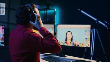Photographer in creative studio working on digital portfolio showcasing photoshoot edited images. Photo editor selecting best photographs while listening music in headphones