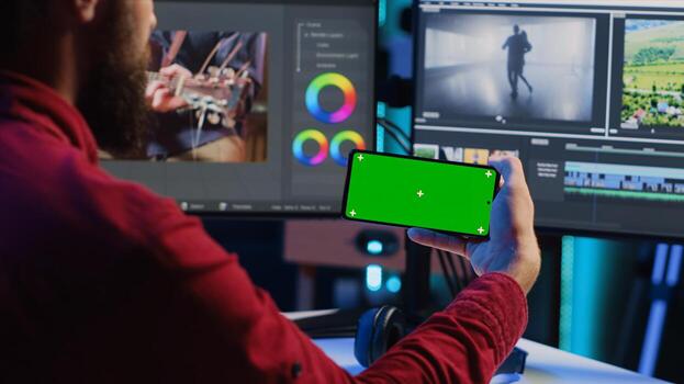 editor watching tutorial on mockup phone about editing color grading and lighting in creative office. Studio employee learning how to work with raw footage on green screen smartphone photo