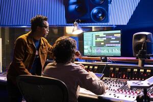 Post production team working on editing sound settings in studio, audio software interface on computer. Artist and sound technician applying mixing and mastering techniques to create a hit. photo