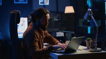 Computer scientist putting headphones on while developing code on PC, making time pass faster during remote job shift. IT admin doing multitasking in home office while listening music, camera A photo