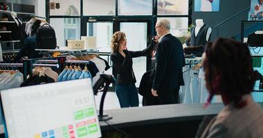 Woman retail clerk showing multiple tie colors to customer, helping him to match formal suit with the perfect accessories. Employee assisting senior client during shopping spree at mall. Camera B. photo