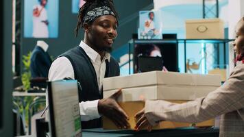 Retail employee picking up clothes order boxes from department store, signing invoice and confirmation papers at cash register counter. African american woman giving requested merchandise. Camera A. photo