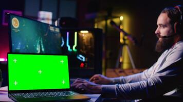 Zoom in on isolated screen laptop next to man using gaming keyboard to play flying singleplayer game. Chroma key notebook and gamer navigating with spacecraft in galaxy, shooting at asteroids photo