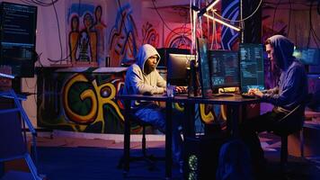 Team of hackers typing fast on keyboards in graffiti painted hideout, rushing to finish developing spyware software in order to use it to gather data from users computers without their knowledge photo