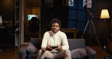 Man focused on playing singleplayer videogames on TV in cozy living room. BIPOC gamer using controller to beat science fiction shooter game on gaming console, relaxing on couch photo