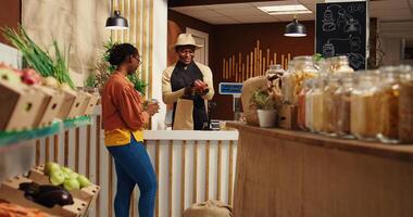 African american seller preparing bag with products for client, weighting fruits and veggies. Merchant scanning bulk items in recyclable jars, woman supporting nonpolluting business. Camera 2. photo
