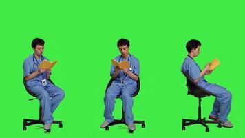 Health specialist is reading a literature book to acquire physician specialization and surgeon expertise, sitting in a chair. Nurse studying healthcare industry lecture against greenscreen. Camera A. photo