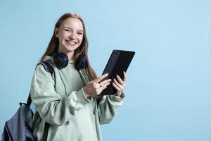 Upbeat teenager using tablet, enjoying funny conversations with friends on text messaging app. Radiant person browsing online web pages on digital device, isolated over studio backdrop photo