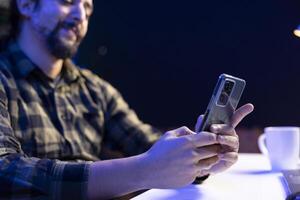Closeup of young man sitting and using his mobile device for communication, chatting with friends. Male individual grasping his smartphone, browsing the internet, checking social media. photo