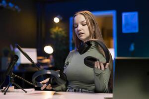 Internet show host holding pair of expensive headphones in hands, doing giveaway for loyal viewers from home studio. Content creator hosting online contest for fans with audio tech as prize photo
