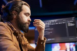 Stressed programmer shutting eyes to relax while fixing vulnerabilities in software systems. Tired man falling asleep at desk from fatigue, using PC to patch security exposures photo