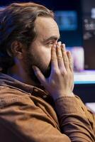 Worried cybersecurity expert putting face in hands after finding many security vulnerabilities, scared of malware infections. Anxious developer distressed by cyber attacks on computer systems photo