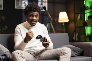 Merry man feeling happy while playing videogames on gaming console with controller, celebrating victory. Player excited after winning game, displaying happiness emotions, shaking fist photo