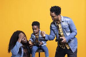 Enthusiastic father playing online games with his baby boy using controller, both parents enjoying leisure time with their small kid. African american happy family play with a joystick. photo