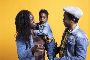 Portrait of african american family with a little child posing on camera, showing gratitude and sympathy towards each other and feeling satisfied. Happy mom and dad holding their boy. photo