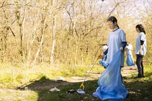 Sweet child volunteer picking up trash and plastic to recycle, working with adults to conserve and restore nature. Little activist combating illegal dumping, collecting rubbish in bags. photo