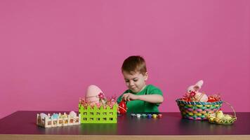 Ecstatic little kid using watercolor and paintbrushes to decorate eggs and create festive baskets as festive arrangements. Happy child enjoys painting and coloring decorations for easter. Camera B. photo