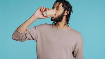 Man enjoys fresh coffee from disposable paper cup early in the morning to wake up and be energized. Person drinks hot beverage from brown recycled takeaway cappuccino cup, studio background, camera B photo