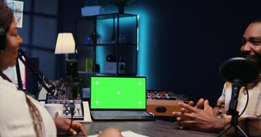Isolated screen laptop next to cohosts streaming podcast using professional vlogging gadgets on internet channel. Chroma key notebook between man and woman meeting in studio to film online show photo