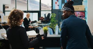 Store assistants receiving new fashion collection to put on display in showroom, looking at clothes from the delivery box at cash register. Employees tea preparing to store new clothing. Camera B. photo