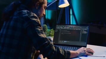 Skilled computer scientist writes code on laptop screen while in living room office using programming languages. Self employed IT specialist working on fixing database errors from home, camera A photo