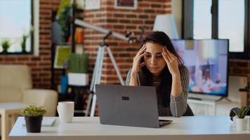 Stressed overworked indian employee struggling to concentrate while working from home, hurting from headache. Tired teleworker feeling nausea while working on laptop, camera B photo