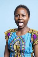 African american joyful person sticking tongue out on camera, fooling around and having fun. Young woman feeling confident and optimistic, making silly goofy facial expressions in studio. photo