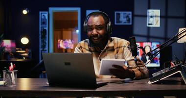 African american media star using outlined ideas on notebook to film vlog channel intro for online streaming platforms. Man following discourse script on paper, presenting today topic photo