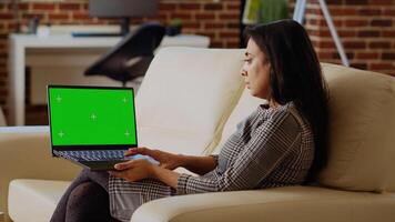 Freelancing businesswoman staying at home using isolated screen laptop to do various job tasks. Remote working indian person typing data on mockup notebook keyboard, sitting on cozy couch photo