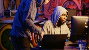 Hacking group new member receiving guidance from knowledgeable rogue programmer acting as his mentor in ghetto abandoned hideaway. Master hacker teaches script kiddie how to deploy viruses photo