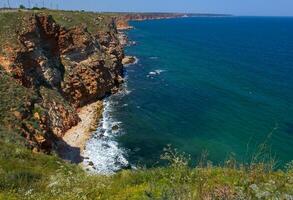 Steep rocky shore and vertical cliffs hanging over the water at Cape Kaliakra photo
