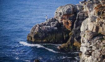 Fisherman on the rock, High inaccessible coastal cliffs made of shell rock photo