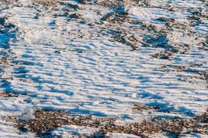 Weathered ice and frozen snow in the form of needle crystals on the bank of the Tiligul Estuary on a sunny day photo