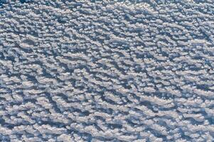 Weathered ice and frozen snow in the form of needle crystals on the bank of the Tiligul Estuary on a sunny day photo