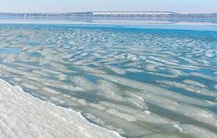 Ice floating near the shore in the form of oblong ice floes, rolled around by waves and a storm in the Tiligul estuary photo