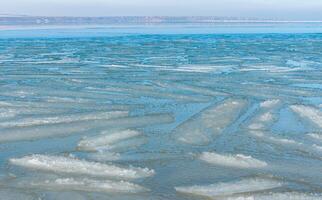 Ice floating near the shore in the form of oblong ice floes, rolled around by waves and a storm in the Tiligul estuary photo