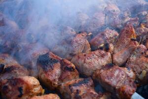 Pork meat is fried on smoking coals in the grill photo