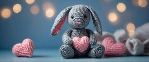 Knitted gray bunny with a crocheted pink hearts on a blue background. photo