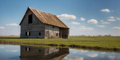 Weathered barn with a deteriorating roof in a green field near a blue water ditch on a sunny spring day. photo
