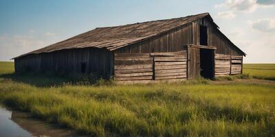 Weathered barn with a deteriorating roof in a green field near a blue water ditch on a sunny spring day. photo