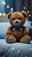 A teddy bear is sitting on a bed with a blue sheet. photo