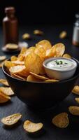 A bowl of chips with a white dip on a black table. photo